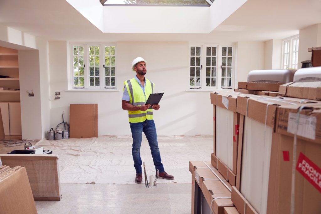 Builder Wearing Hard Hat With Clipboard Checking Delivery Of New Kitchen Units Inside Property